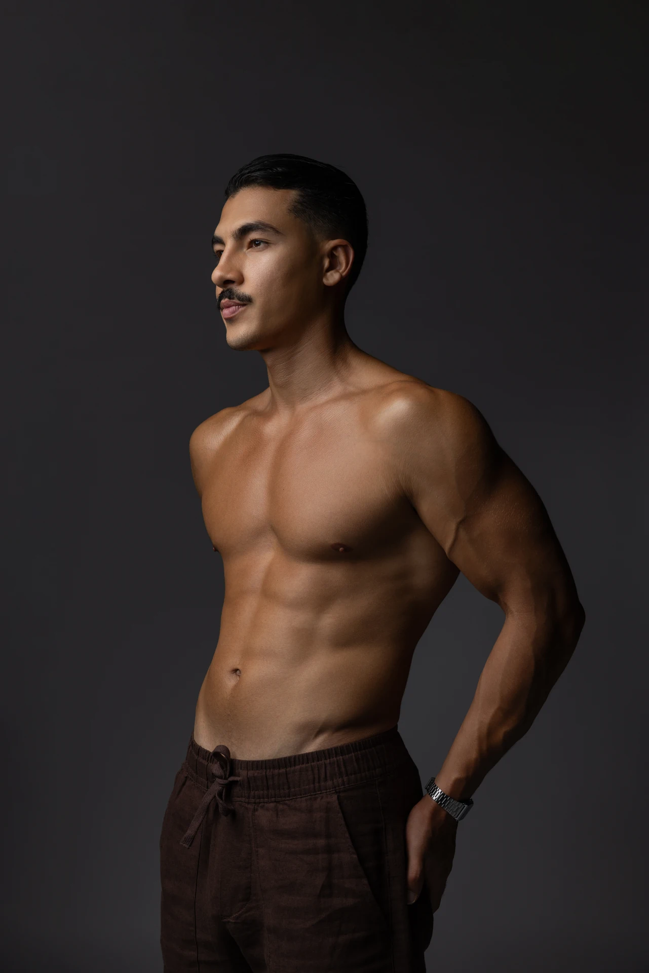 Shirtless three quarter portrait in brown trousers with dramatic side light. Male modeling portfolio photoshoot by MRPS in Dubai, photographed by Nastaran.