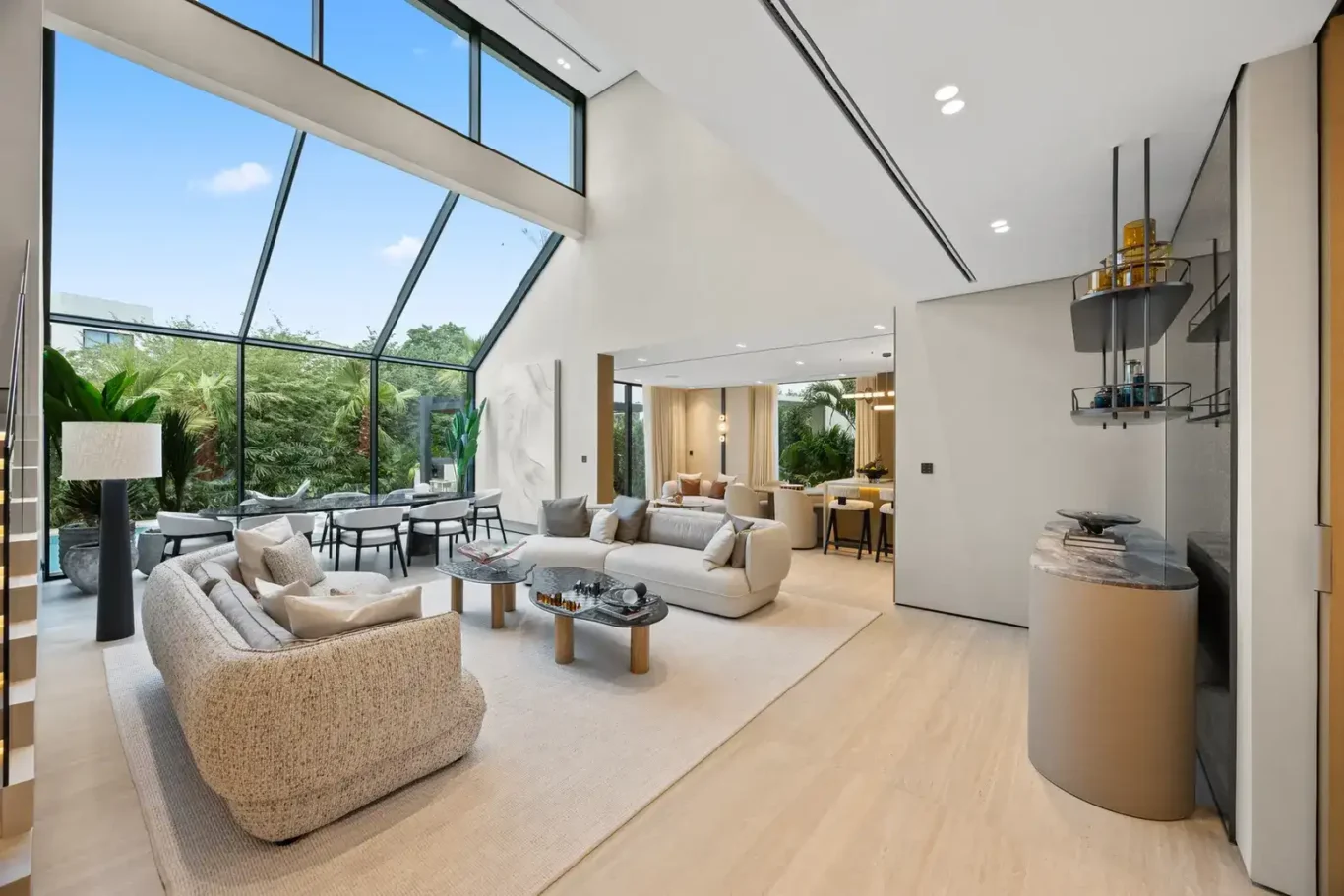 Double-height living room with curved sofas and a slanted glass wall, luxury villa in Jumeirah Islands, Dubai.