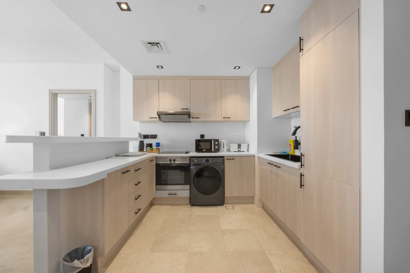 Fitted kitchen with oven, washer and wood cabinets in a Your Stay Apartments one-bedroom at Sky Gardens, DIFC, Dubai.