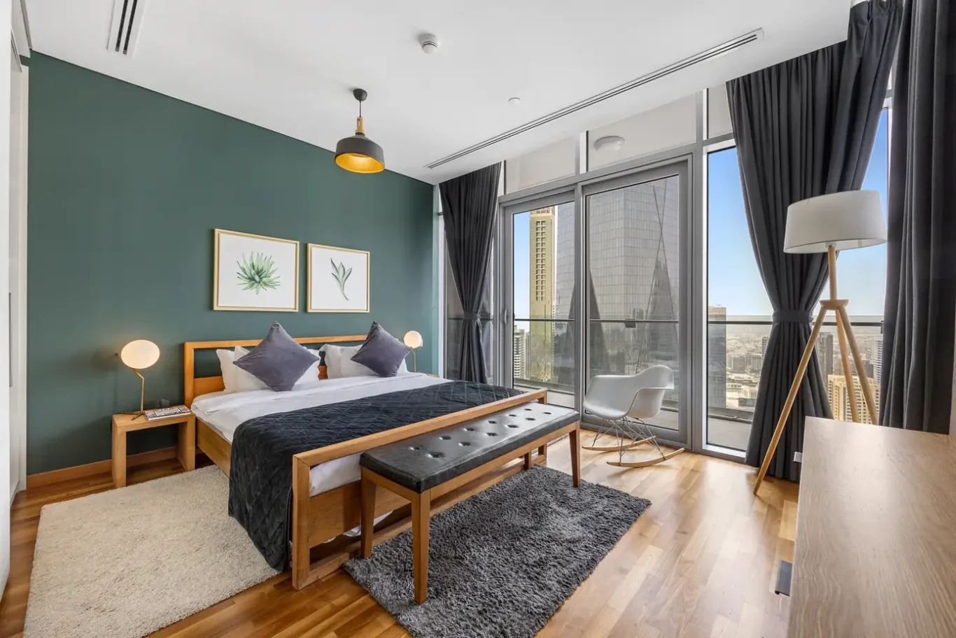 Bedroom with king bed, green feature wall and full-height windows in a Your Stay Apartments one-bedroom at Burj Daman, DIFC, Dubai.