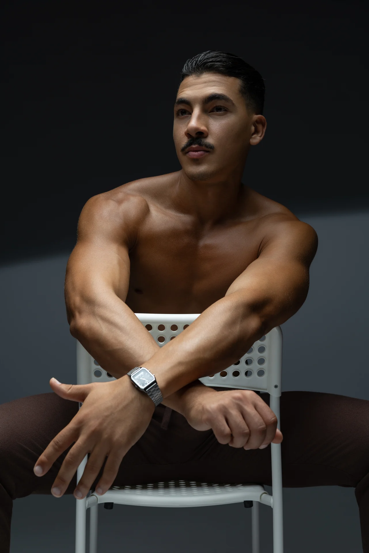 Seated backwards on a white chair, shirtless, arms resting on the chair back. Male modeling portfolio photoshoot by MRPS in Dubai, photographed by Nastaran.