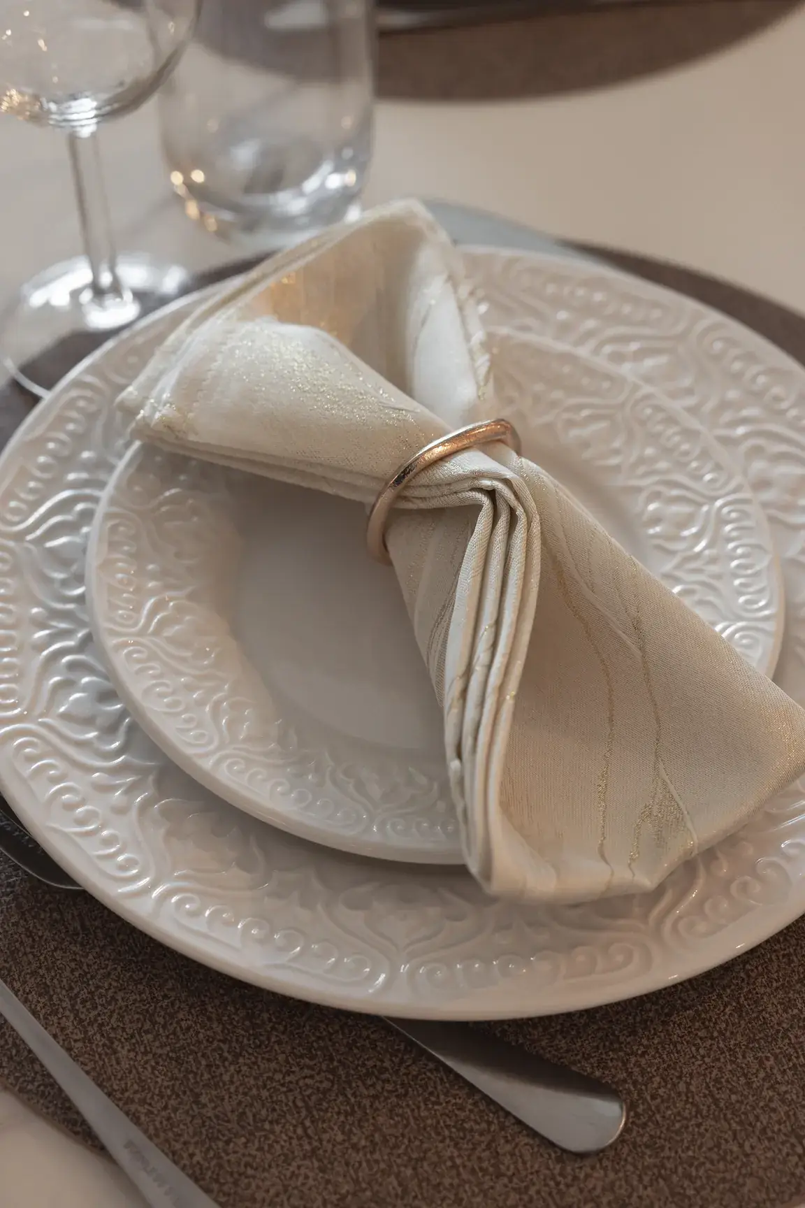 Table setting detail with embossed plates and a ringed linen napkin. Interior design photography for Aziza Home by MRPS in Dubai.