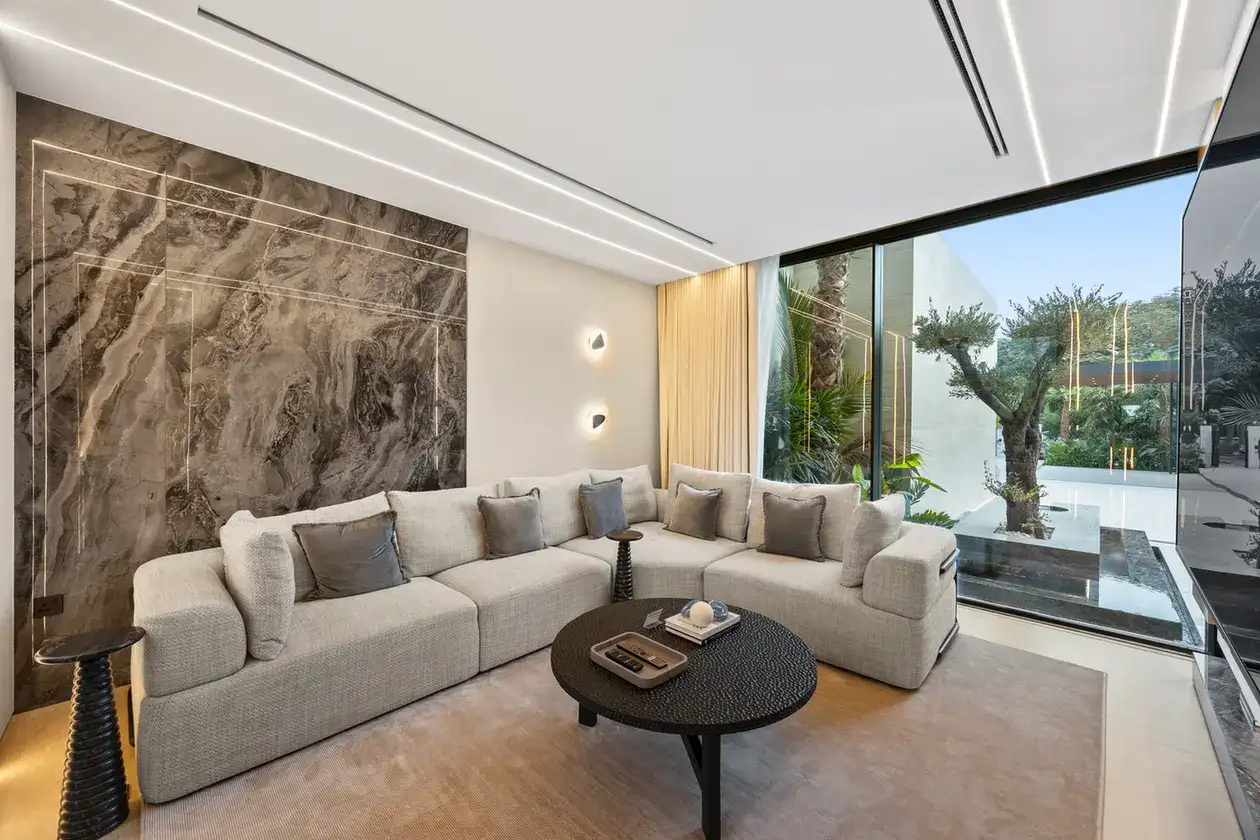 TV lounge with a marble feature wall and a sectional sofa, luxury villa in Jumeirah Islands, Dubai.