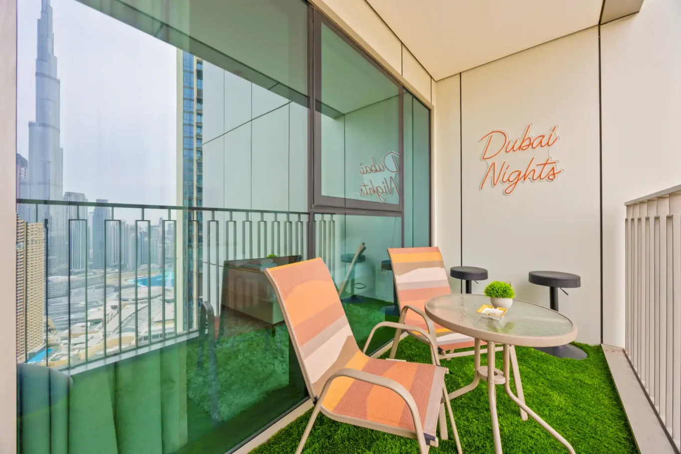 Balcony with artificial grass, bistro chairs and a Dubai Nights neon sign. Day, twilight and night Airbnb photography by MRPS for Vista Haus Holiday Homes in Downtown Dubai.