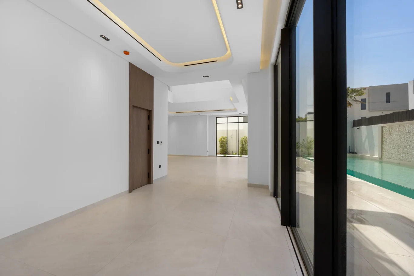 Living area with full-height glass doors and the pool outside, unfurnished five-bedroom villa in Al Furjan, Dubai.