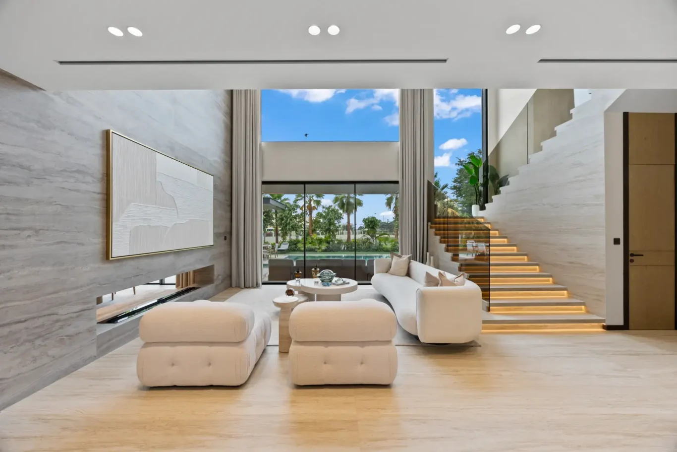Double-height living room with cream armchairs, a floating staircase and garden view, luxury villa in Jumeirah Islands, Dubai.