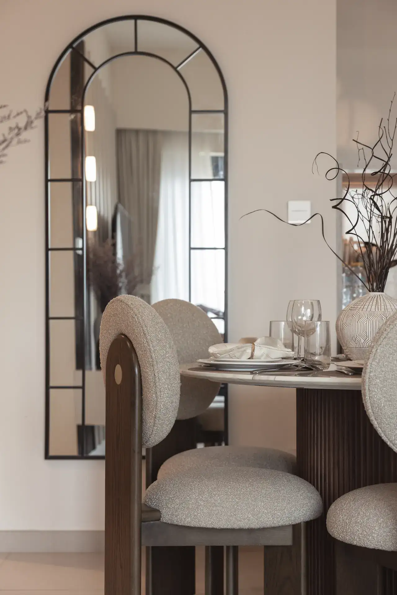 Dining corner with an arched black mirror and boucle chairs. Interior design photography for Aziza Home by MRPS in Dubai.