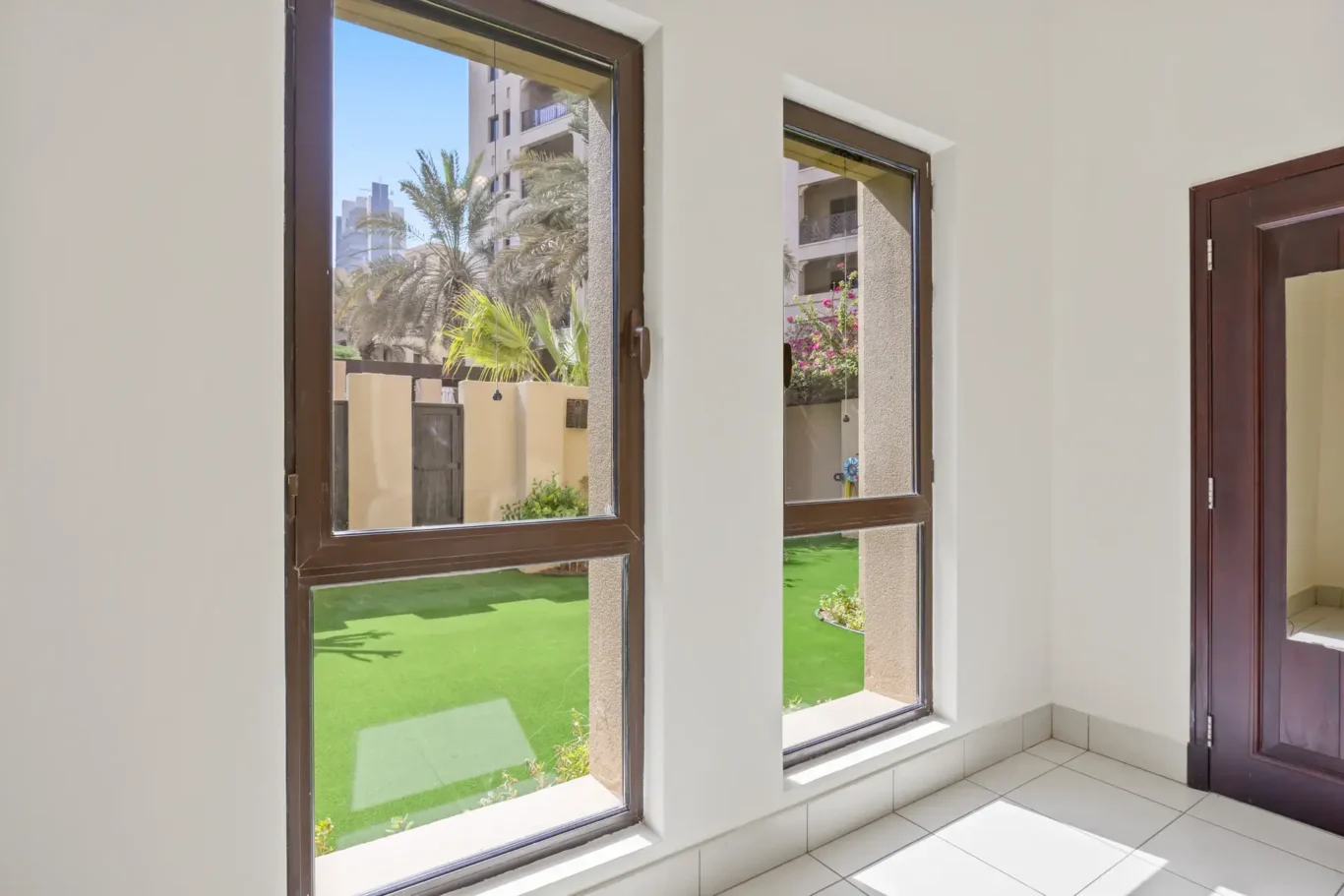 Tall windows looking onto the green garden in an unfurnished two-bedroom garden apartment in Old Town, Downtown Dubai, photographed for ELITE Property Brokerage.