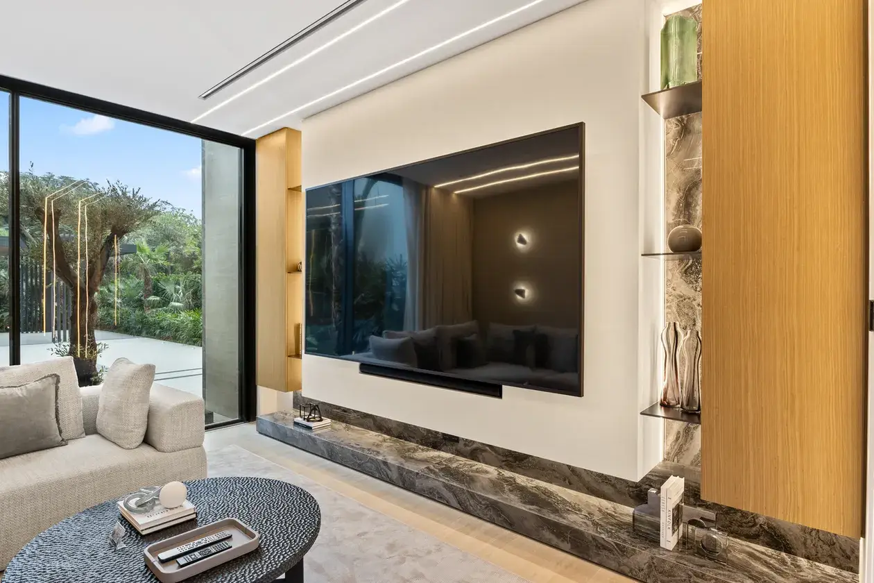 TV lounge sofa with a garden view through tall windows, luxury villa in Jumeirah Islands, Dubai.