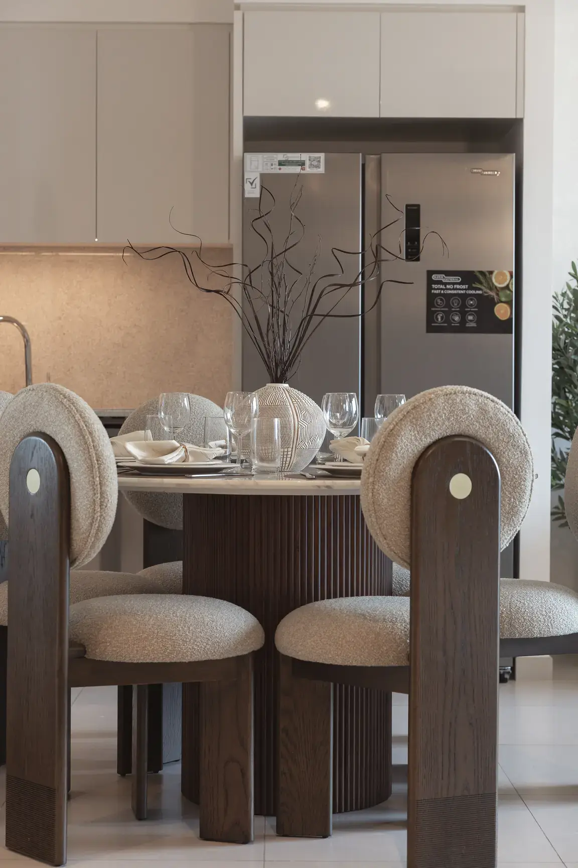 Round dining table with boucle chairs in front of the open kitchen. Interior design photography for Aziza Home by MRPS in Dubai.