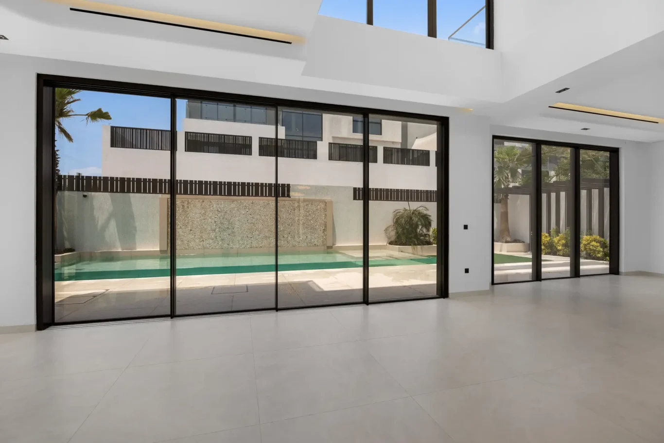 Living room glass wall facing the pool and mosaic water wall, unfurnished five-bedroom villa in Al Furjan, Dubai.