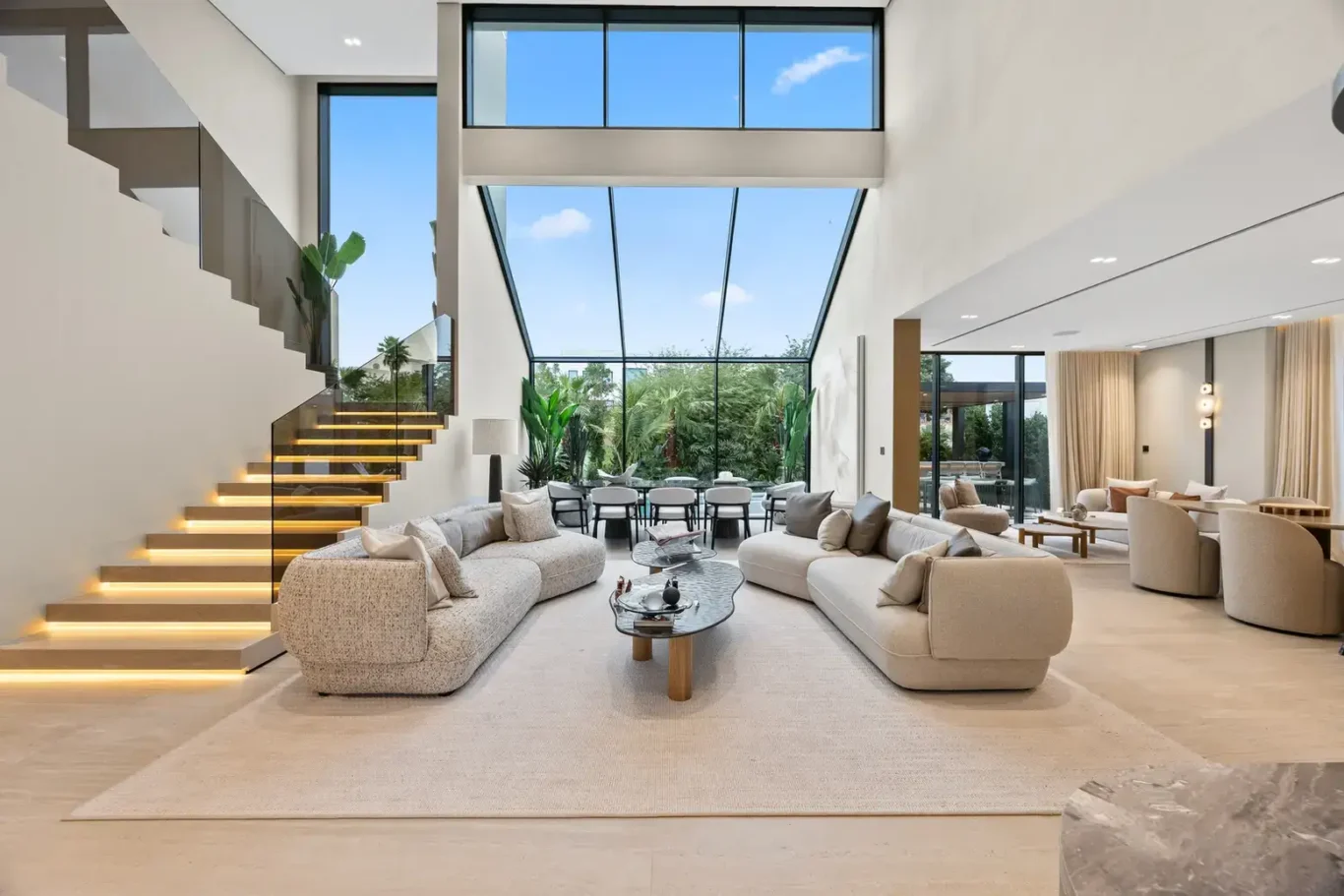 Double-height living and dining area with the staircase and glass wall, luxury villa in Jumeirah Islands, Dubai.