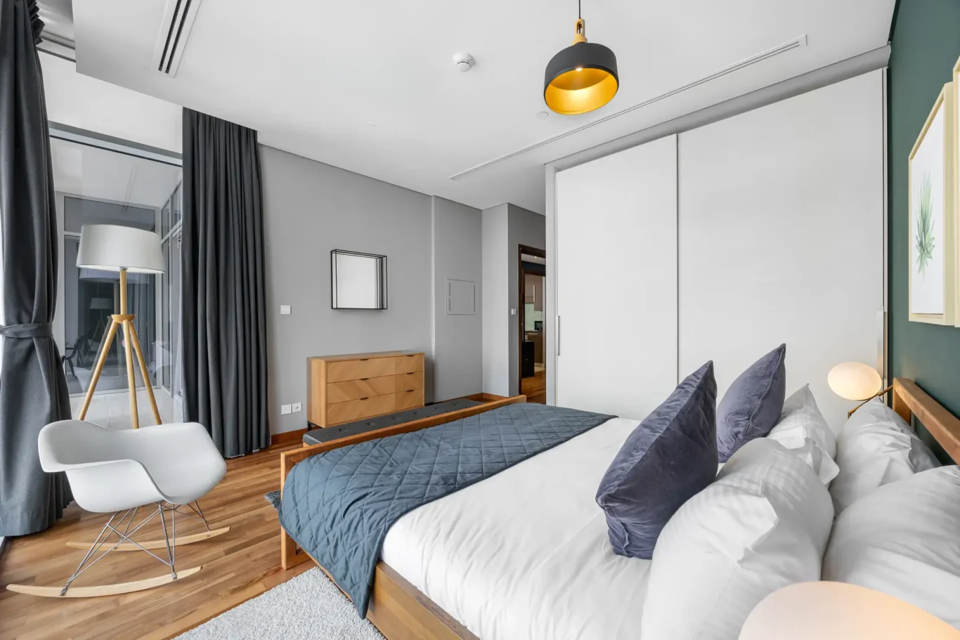Bedroom with reading chair and floor lamp in a Your Stay Apartments one-bedroom at Burj Daman, DIFC, Dubai.