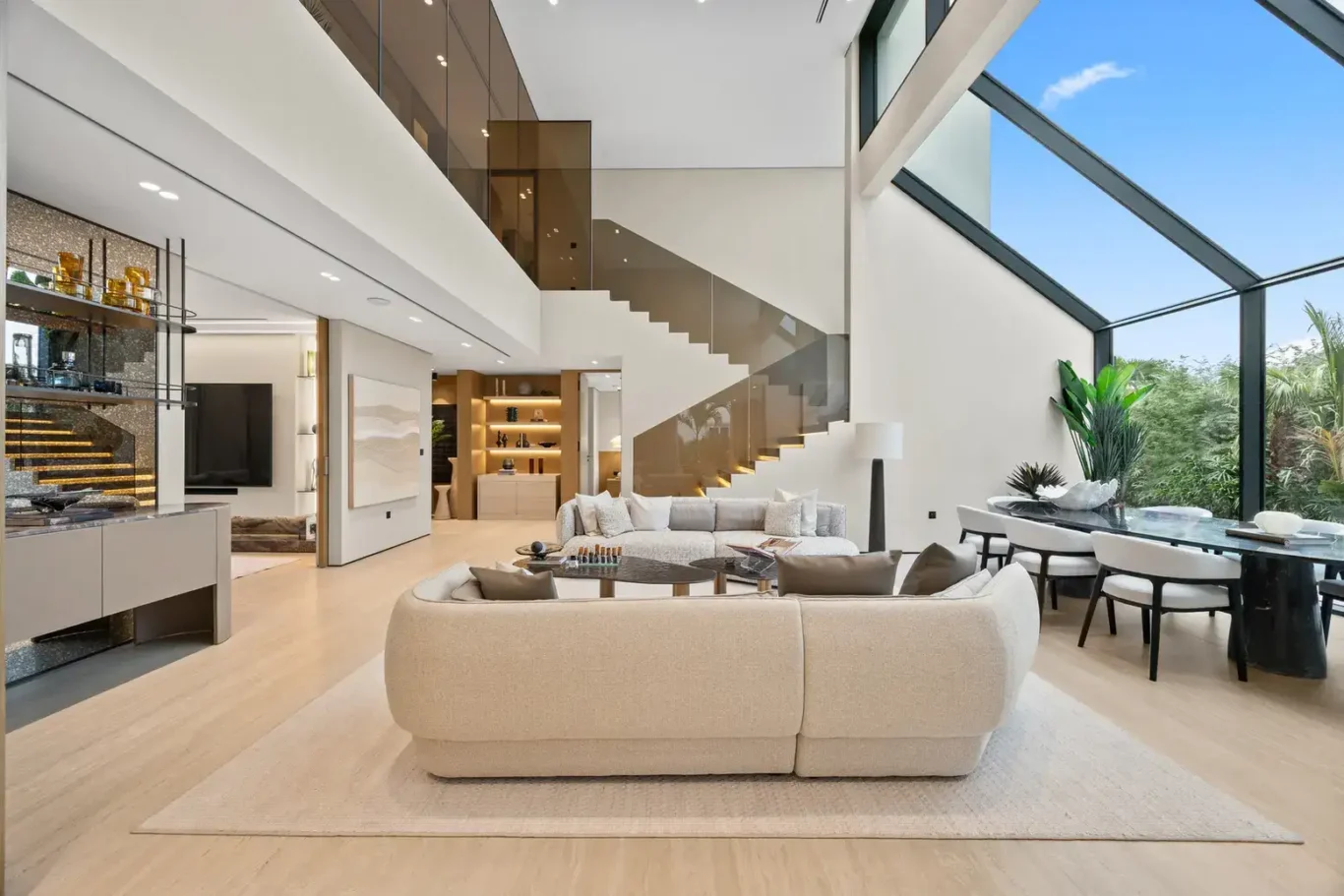 Living room with curved sofas beneath a floating staircase, luxury villa in Jumeirah Islands, Dubai.