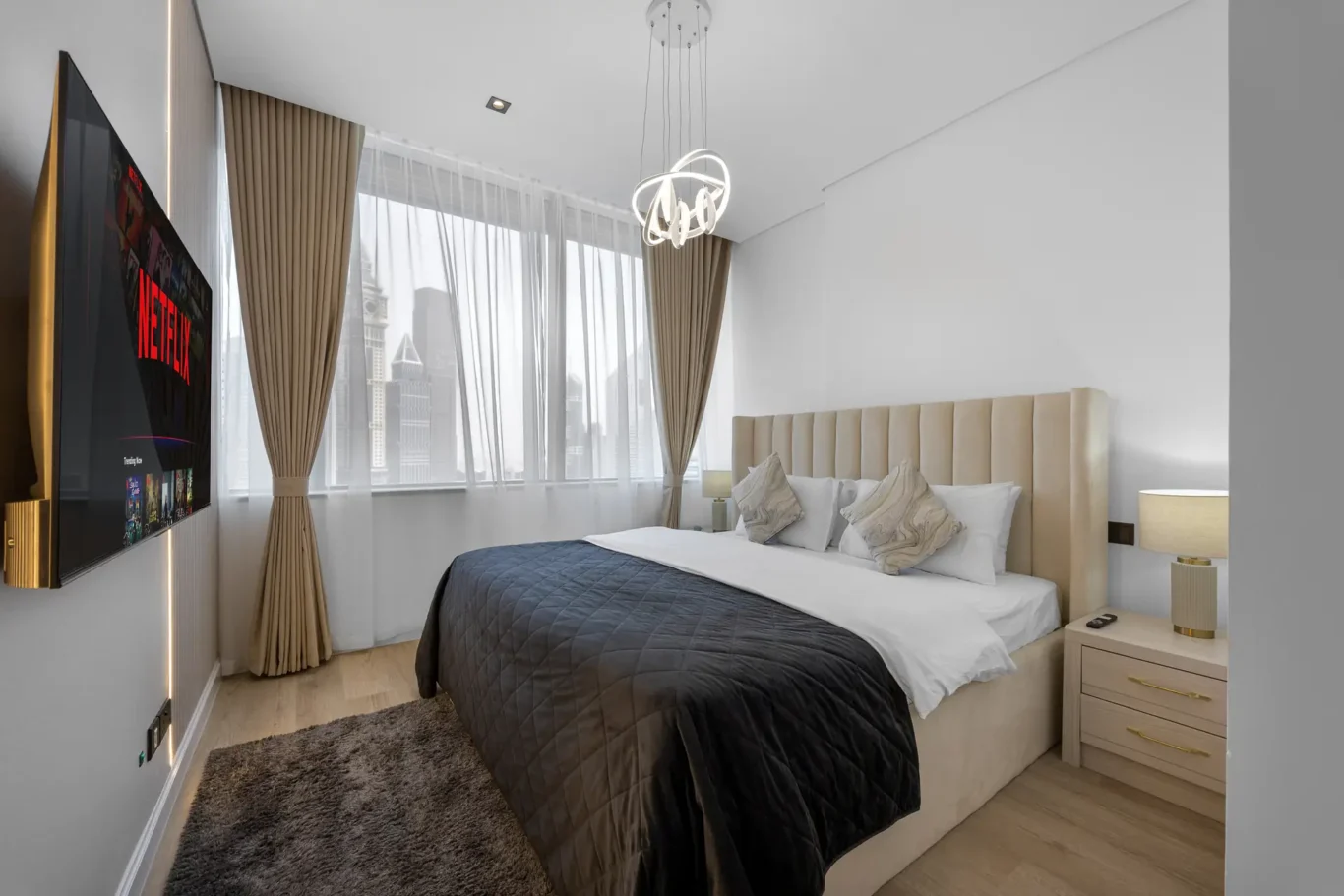 Bedroom with upholstered bed, TV and city view in a Your Stay Apartments one-bedroom at Sky Gardens, DIFC, Dubai.