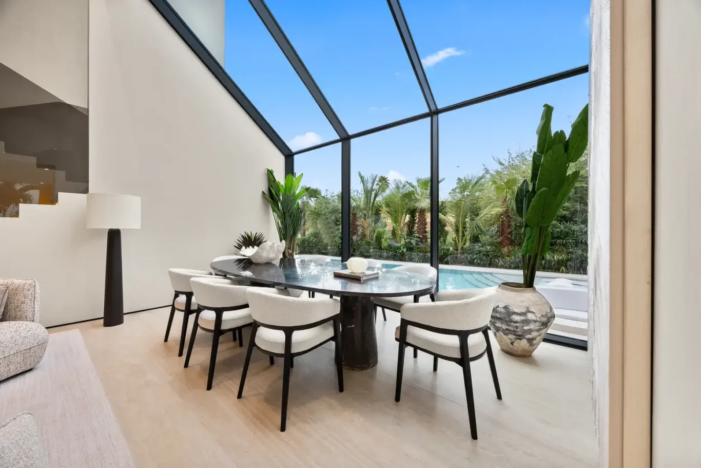 Dining table with white chairs beside a glass wall and pool view, luxury villa in Jumeirah Islands, Dubai.