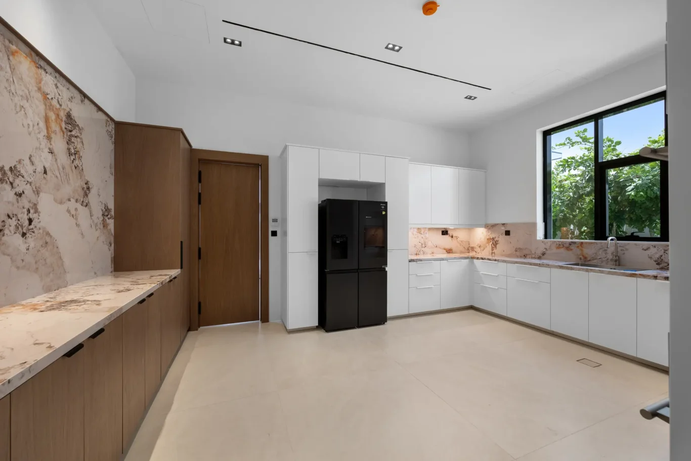 Kitchen with a marble splashback, walnut cabinets and a black fridge, unfurnished five-bedroom villa in Al Furjan, Dubai.
