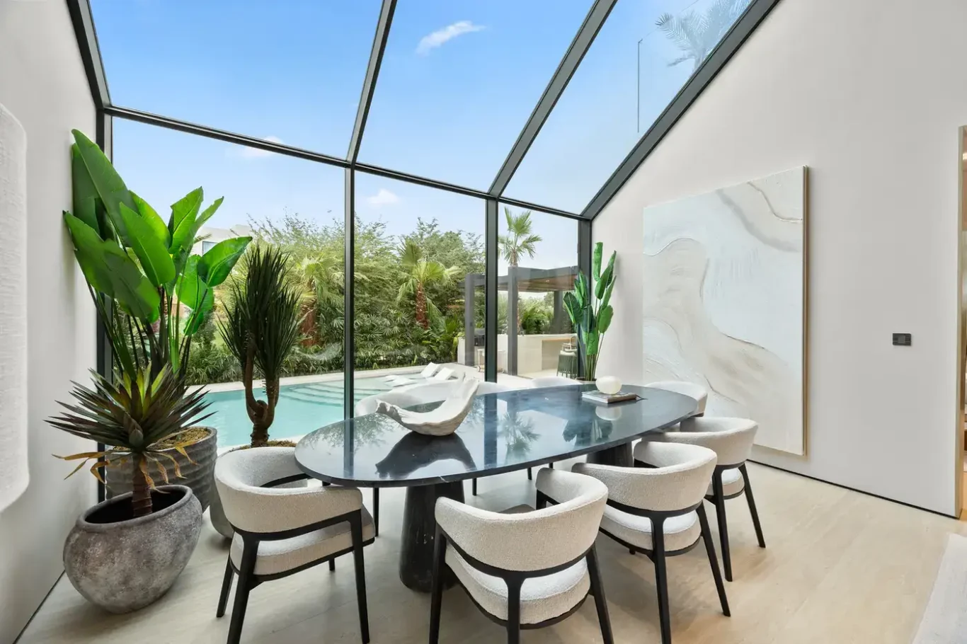 Dining table beside the slanted glass wall with the pool outside, luxury villa in Jumeirah Islands, Dubai.