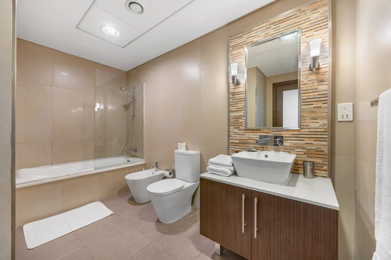 Bathroom with bathtub, vanity and stone mosaic in a Your Stay Apartments one-bedroom at Burj Daman, DIFC, Dubai.