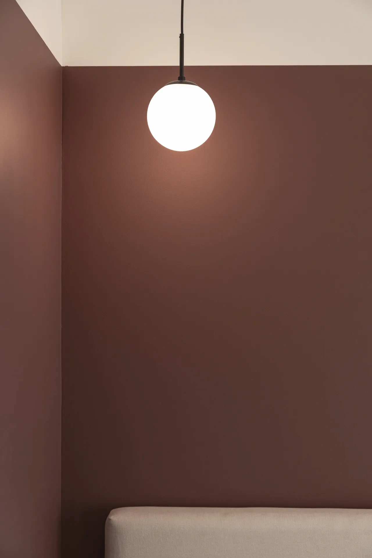 Terracotta painted wall with a glass globe pendant light. Interior design photography for Aziza Home by MRPS in Dubai.