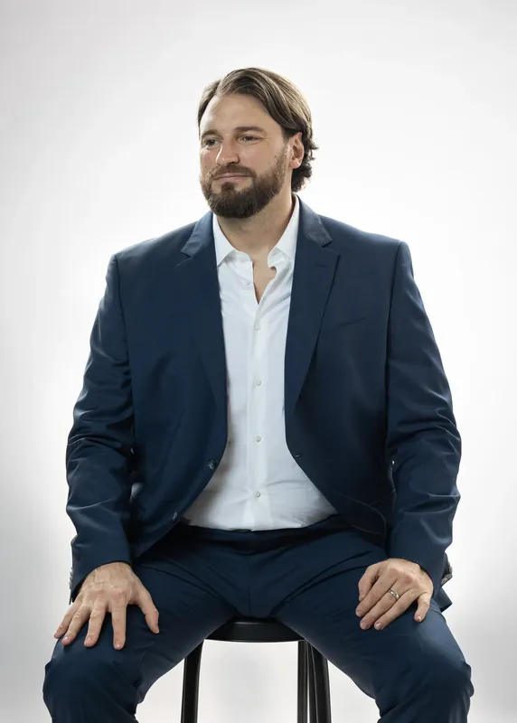Seated on a stool, facing the camera. White background reference photo from an AI model training photoshoot at the MRPS studio in Dubai.