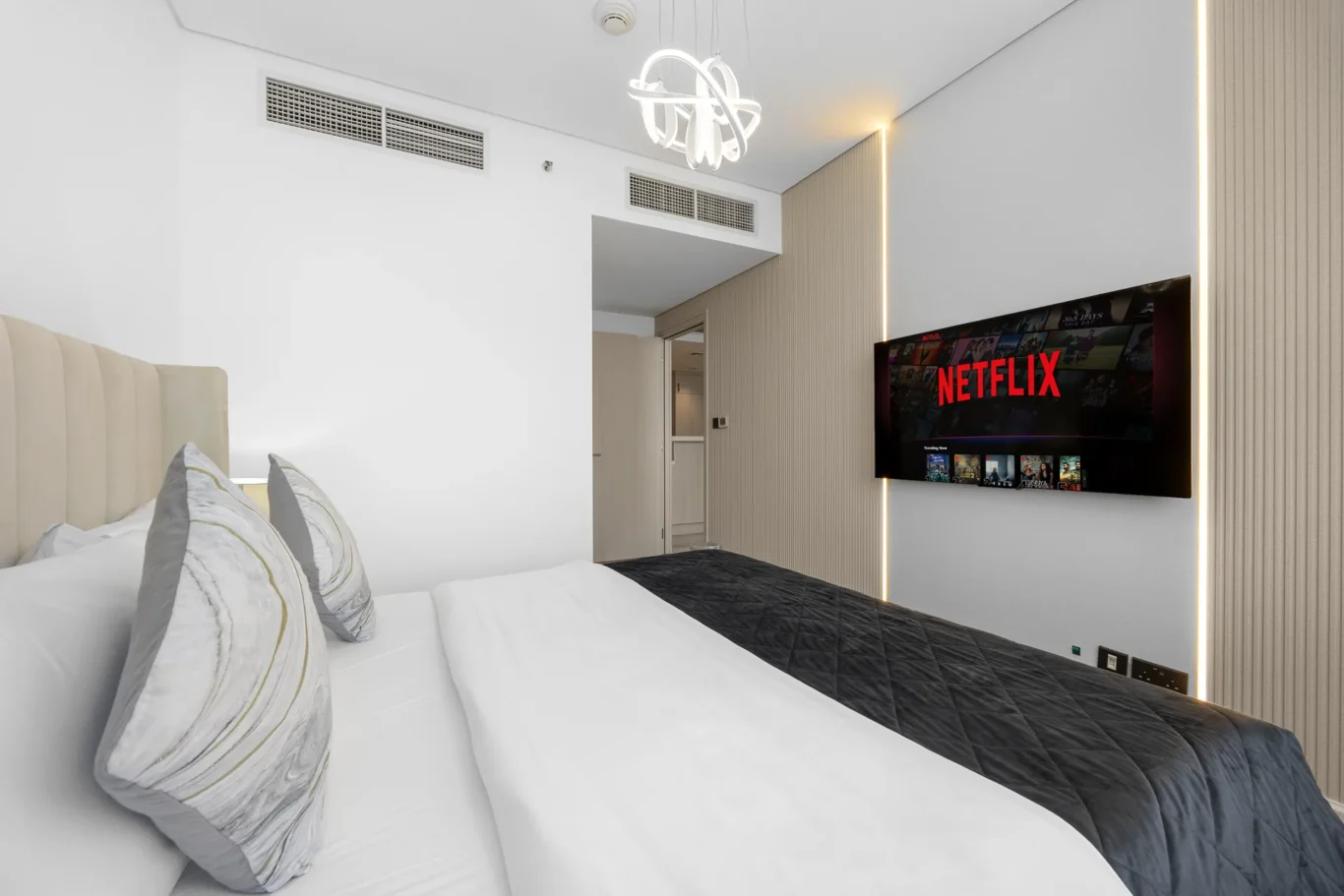 Bed with chandelier and smart TV in a Your Stay Apartments one-bedroom at Sky Gardens, DIFC, Dubai.