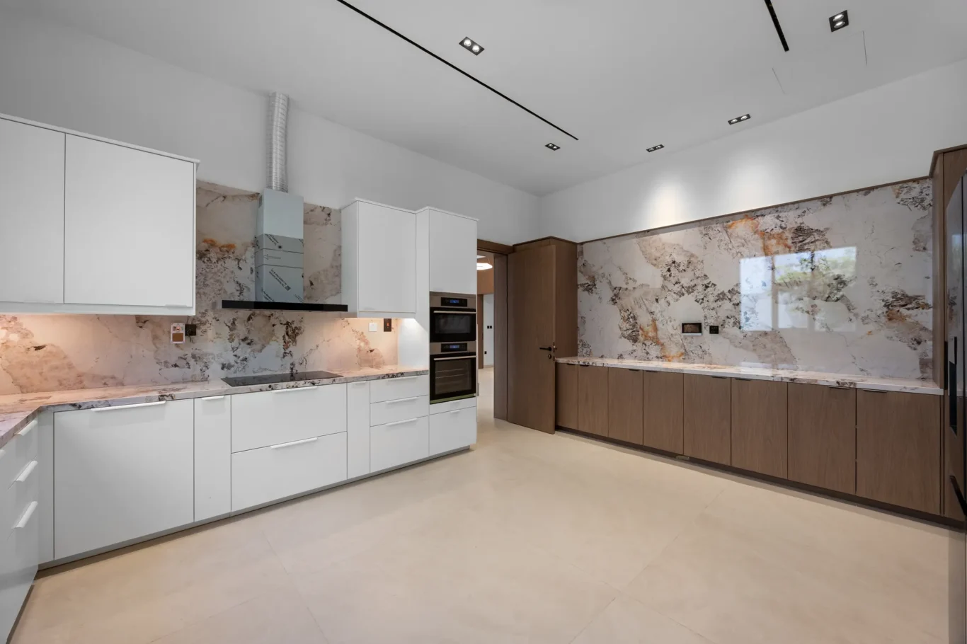 Kitchen hob and white wall units with a marble splashback, unfurnished five-bedroom villa in Al Furjan, Dubai.