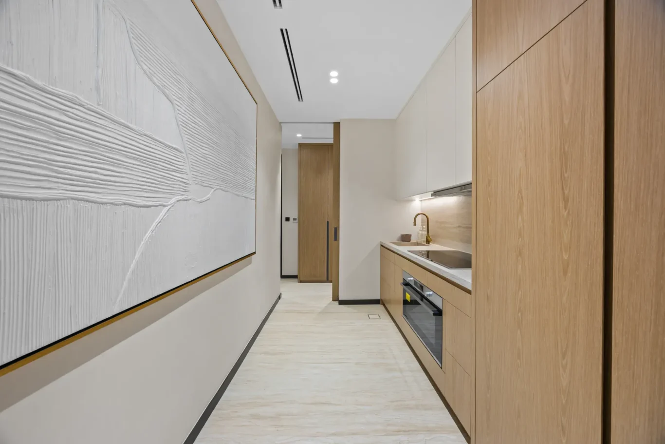 Service kitchen with wood cabinetry and textured wall art in the corridor, luxury villa in Jumeirah Islands, Dubai.