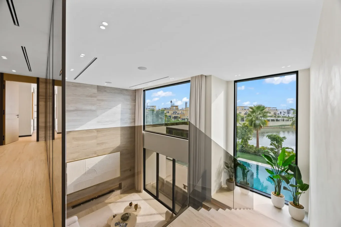 Upper landing with a glass balustrade overlooking the living room and pool, luxury villa in Jumeirah Islands, Dubai.