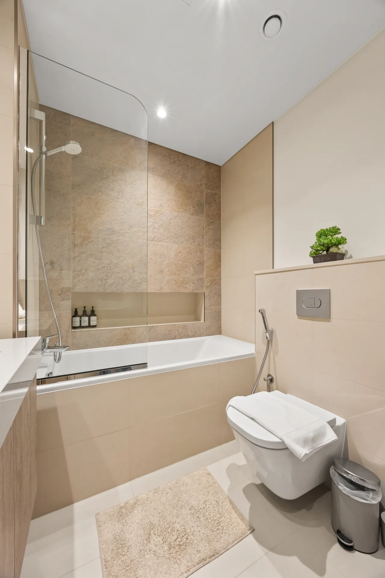 Second bathroom bathtub with stone tiles and wall hung toilet. Day, twilight and night Airbnb photography by MRPS for Vista Haus Holiday Homes in Downtown Dubai.