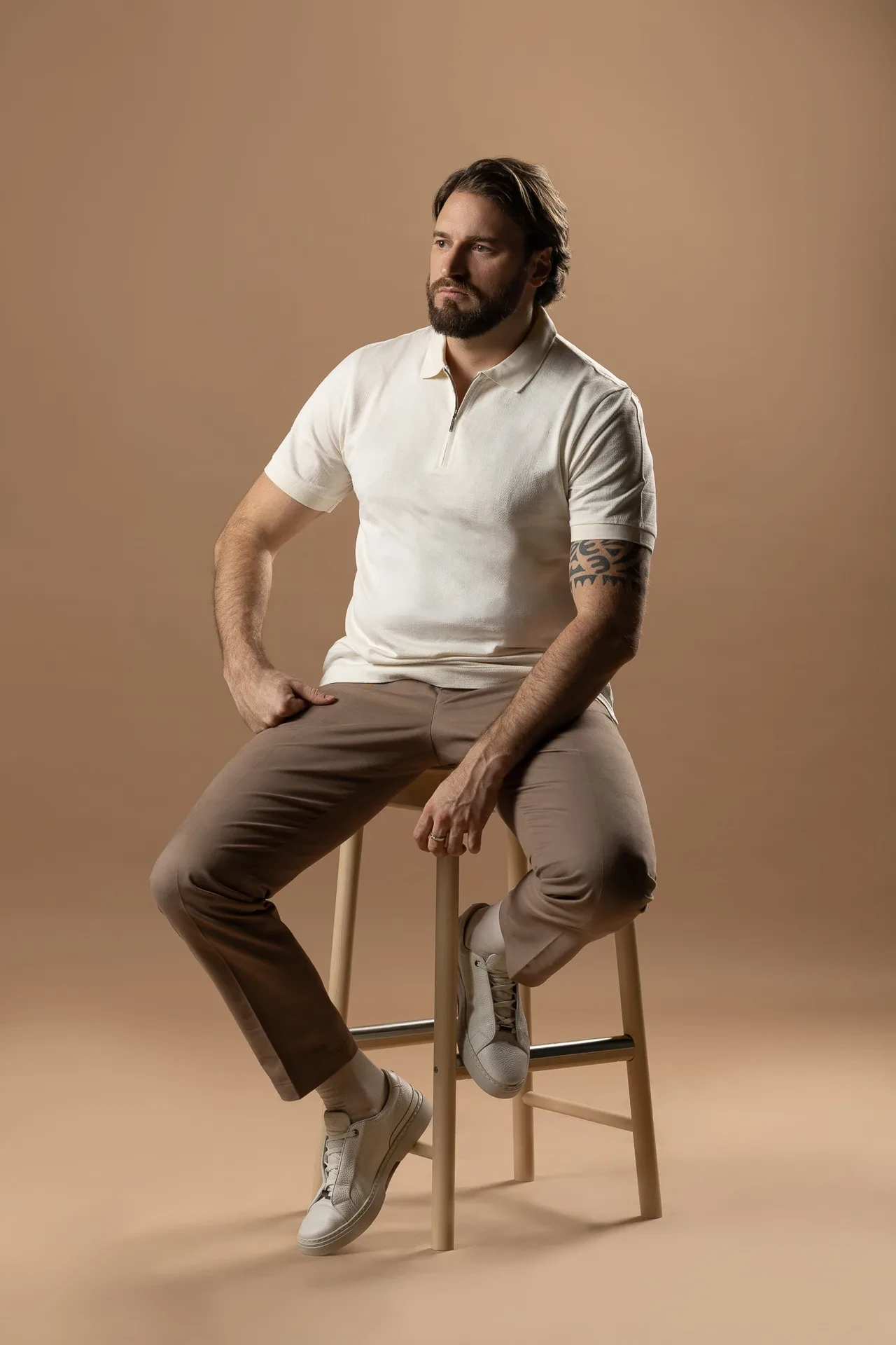 Casual seated portrait in a white knit polo on a beige backdrop. Lifestyle portrait from an AI digital twin photoshoot at the MRPS studio in Dubai.