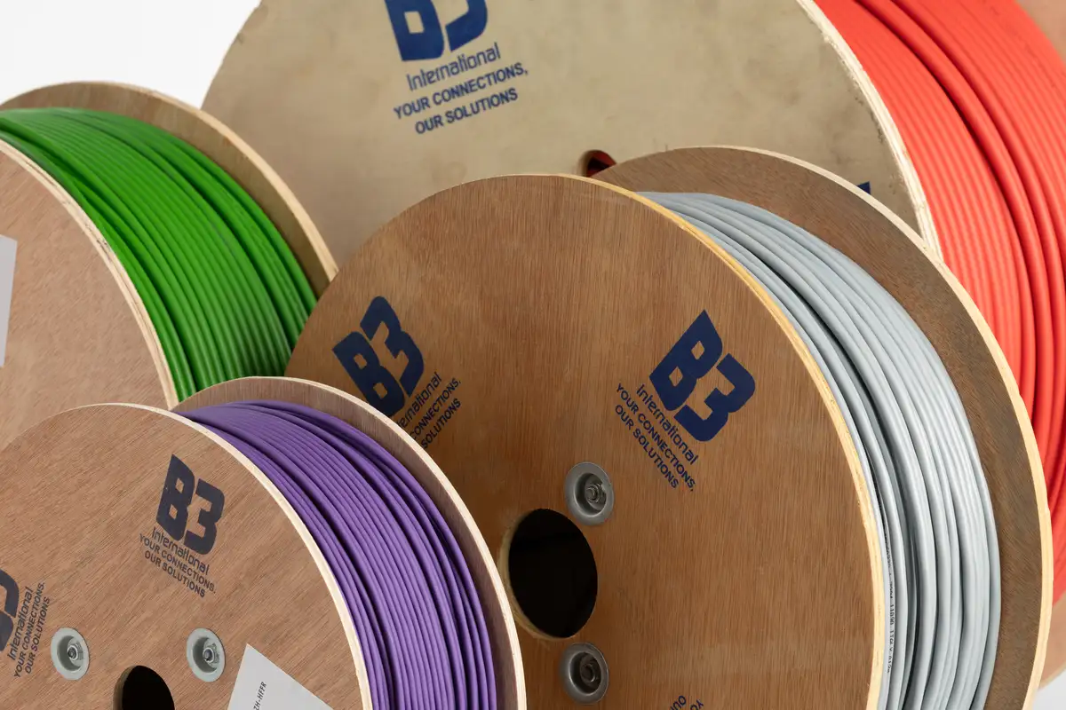 Close view of B3 International wooden cable drums with printed logo and green, purple, grey and red cable.