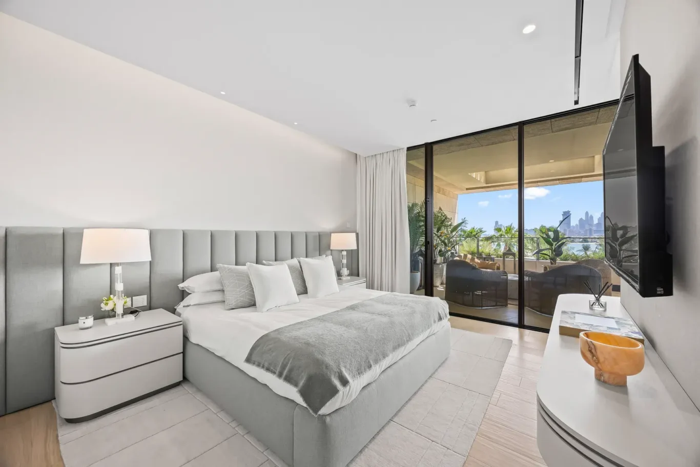Guest bedroom with grey upholstered bed and garden view in a furnished three-bedroom residence at Atlantis The Royal, Palm Jumeirah, photographed for Apex Homes Real Estate.