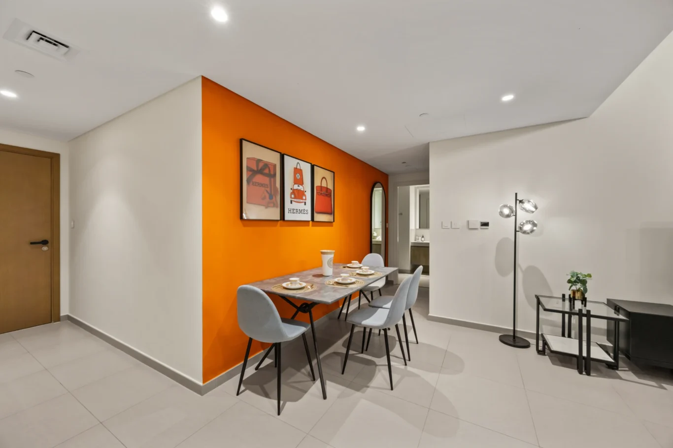 Dining area with orange wall, pendant lights and the living room beyond. Day, twilight and night Airbnb photography by MRPS for Vista Haus Holiday Homes in Downtown Dubai.