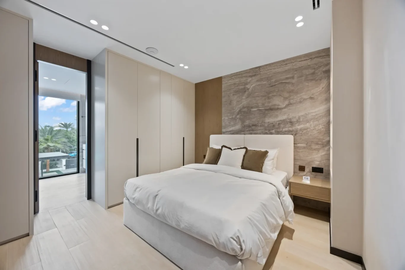 Bedroom with a stone feature wall, white bed and balcony access, luxury villa in Jumeirah Islands, Dubai.