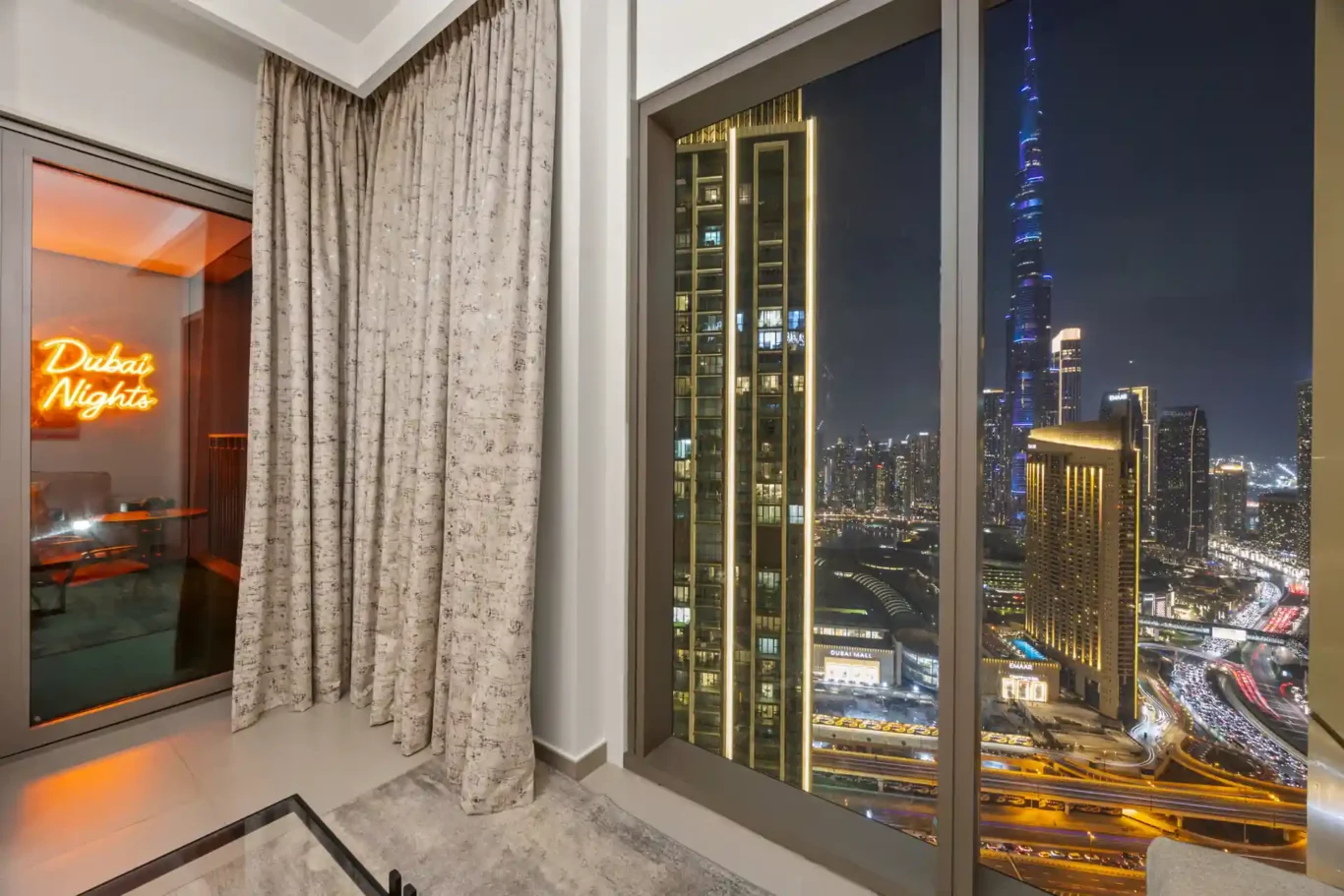 Living room at twilight with the balcony neon sign and TV wall. Day, twilight and night Airbnb photography by MRPS for Vista Haus Holiday Homes in Downtown Dubai.