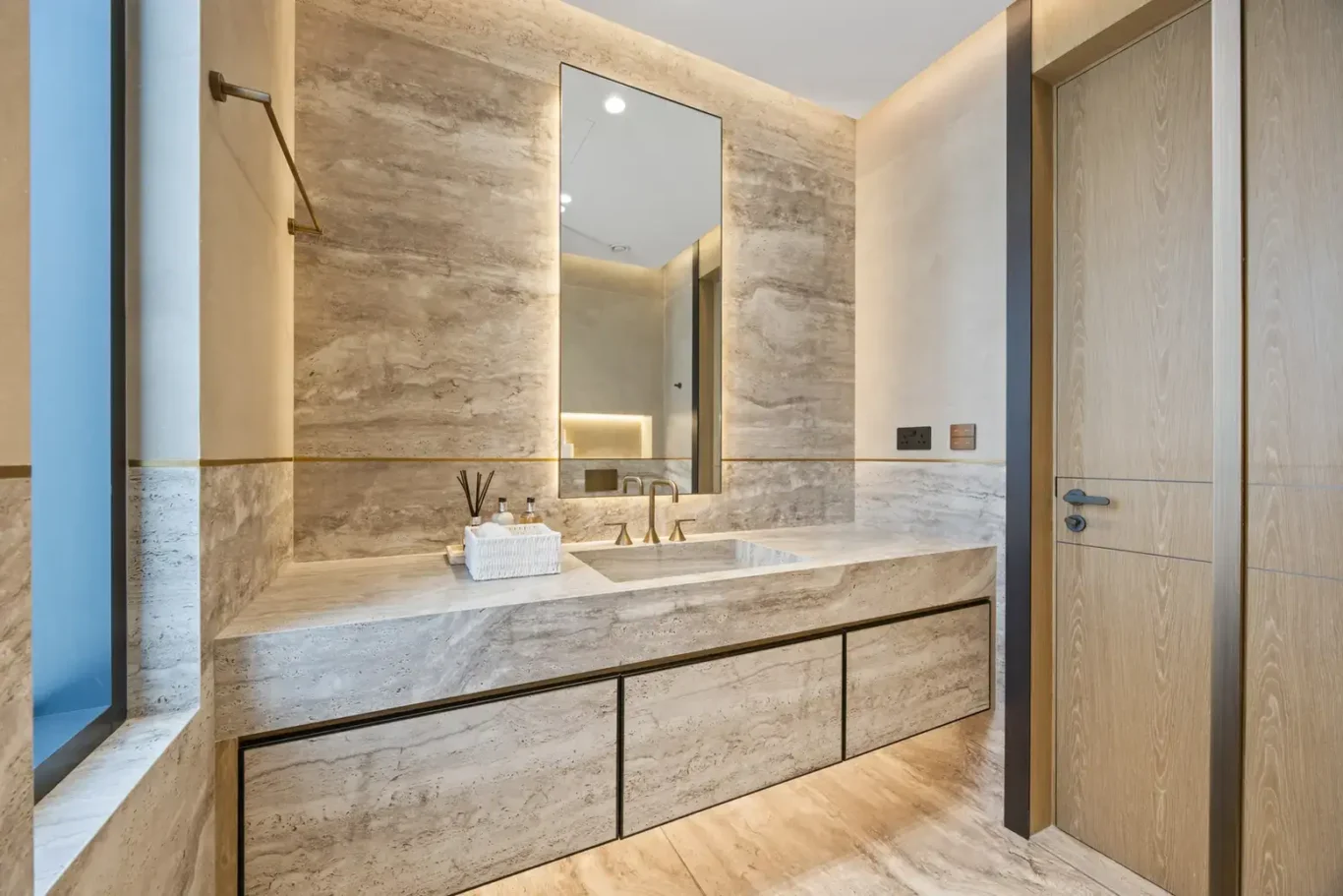 Bathroom with a stone vanity, lit mirror and wood door, luxury villa in Jumeirah Islands, Dubai.