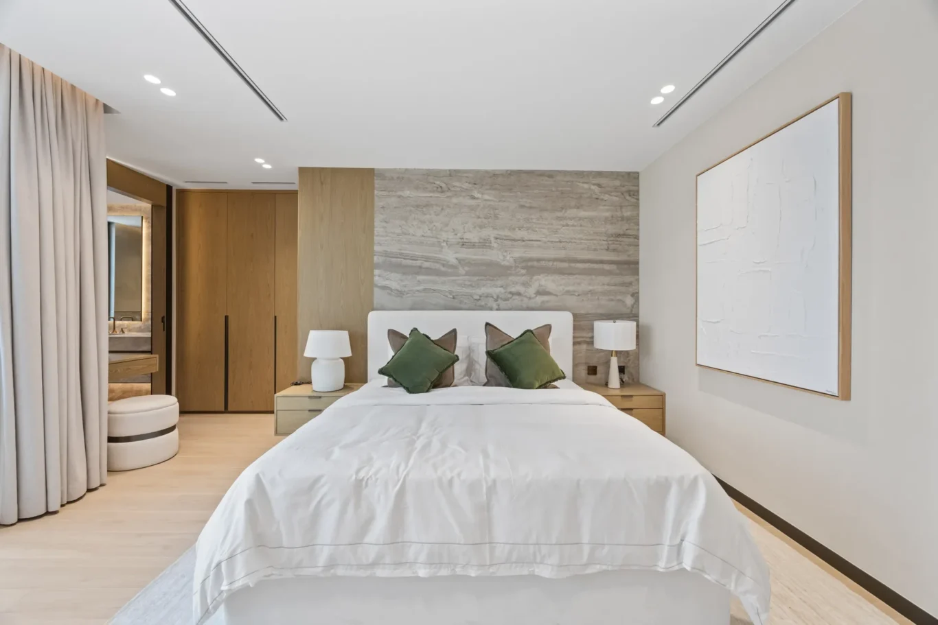 Master bedroom with a white bed, stone headboard wall and artwork, luxury villa in Jumeirah Islands, Dubai.