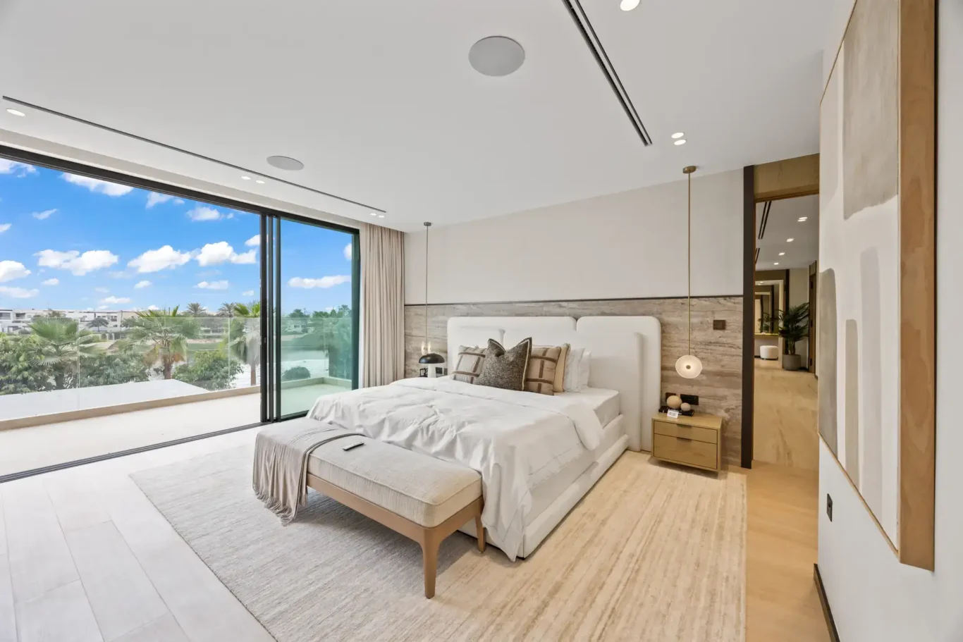 Master bedroom with a bench at the foot of the bed and a terrace view, luxury villa in Jumeirah Islands, Dubai.
