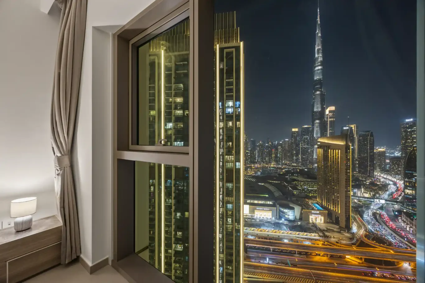 King bed at twilight with the Burj Khalifa lit up outside. Day, twilight and night Airbnb photography by MRPS for Vista Haus Holiday Homes in Downtown Dubai.