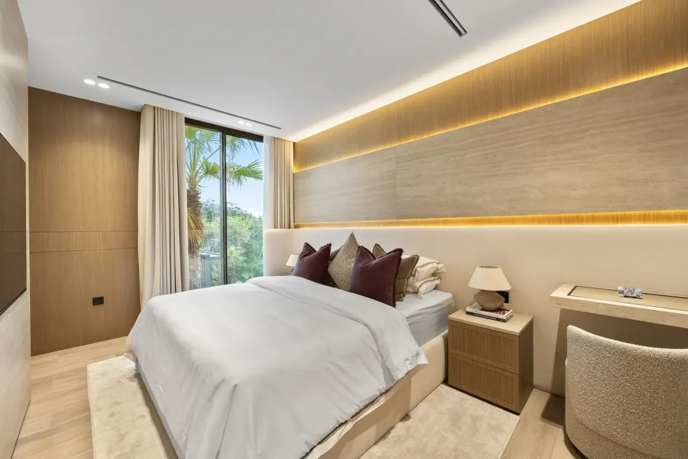 Bedroom with a lit wood headboard wall and garden view, luxury villa in Jumeirah Islands, Dubai.
