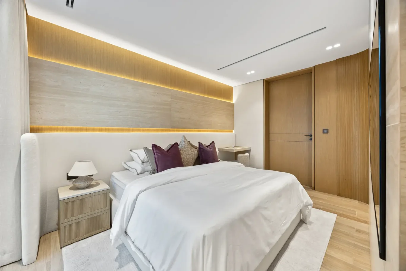 Bedroom bed with burgundy cushions and a bedside lamp, luxury villa in Jumeirah Islands, Dubai.