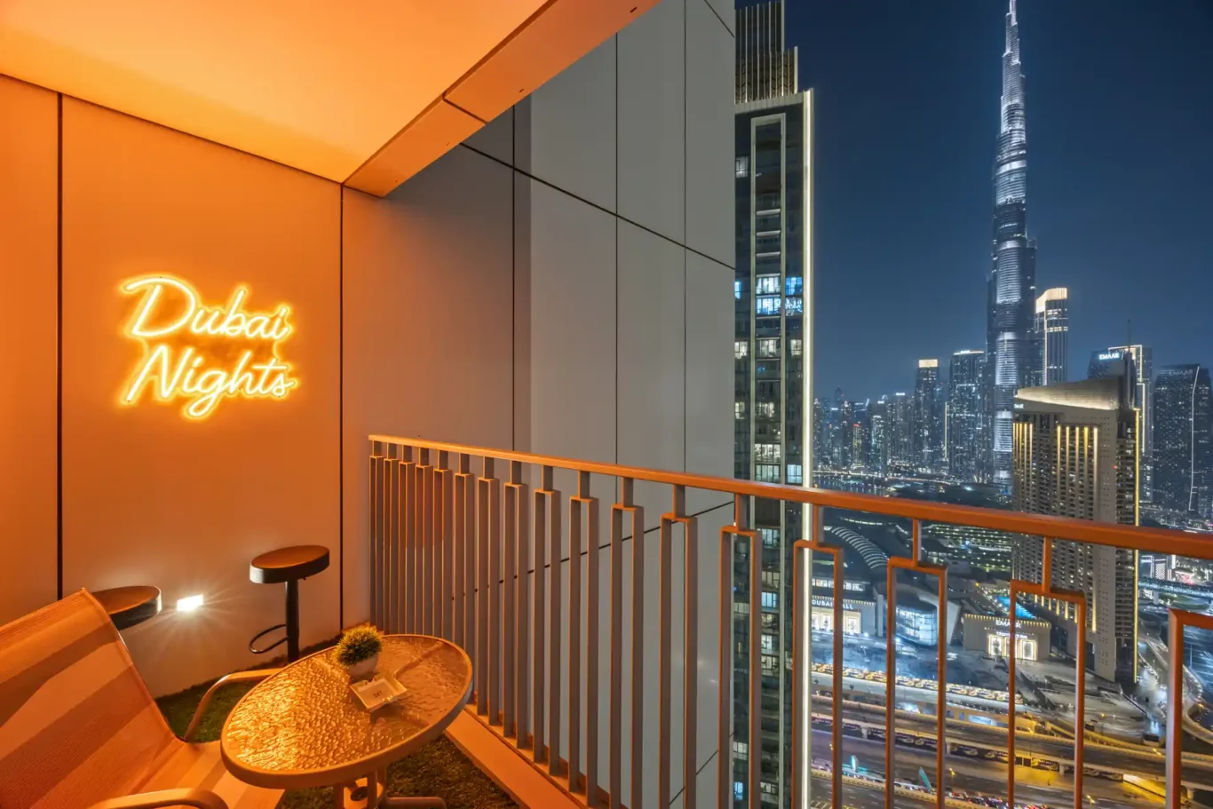 Balcony at night with bistro chairs, neon sign and the lit up skyline. Day, twilight and night Airbnb photography by MRPS for Vista Haus Holiday Homes in Downtown Dubai.