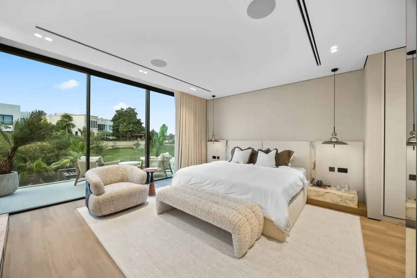 Master bedroom with a boucle armchair, bench and tall windows, luxury villa in Jumeirah Islands, Dubai.