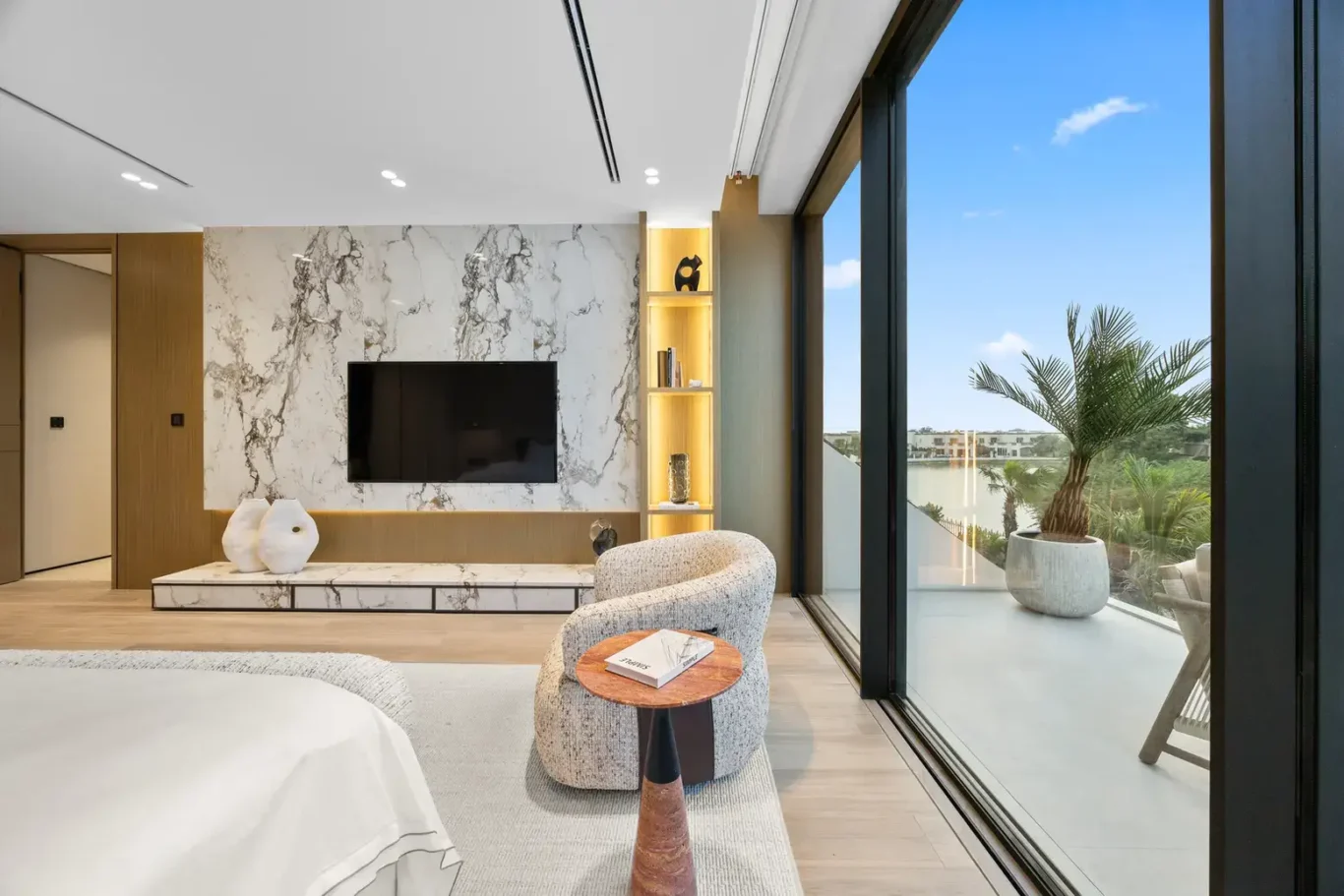Master bedroom seating area with a marble TV wall and terrace door, luxury villa in Jumeirah Islands, Dubai.