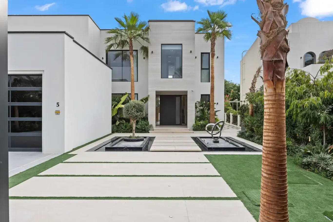 Modern white front facade with palm trees and a stone pathway, luxury villa in Jumeirah Islands, Dubai.