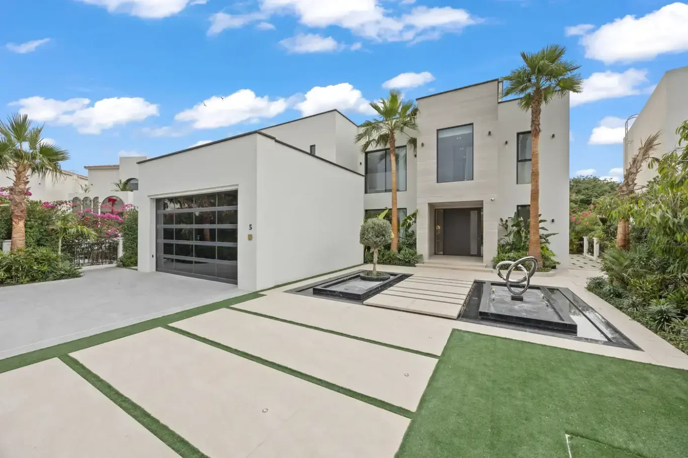 Front exterior of the modern villa with a glass garage door and water features, luxury villa in Jumeirah Islands, Dubai.