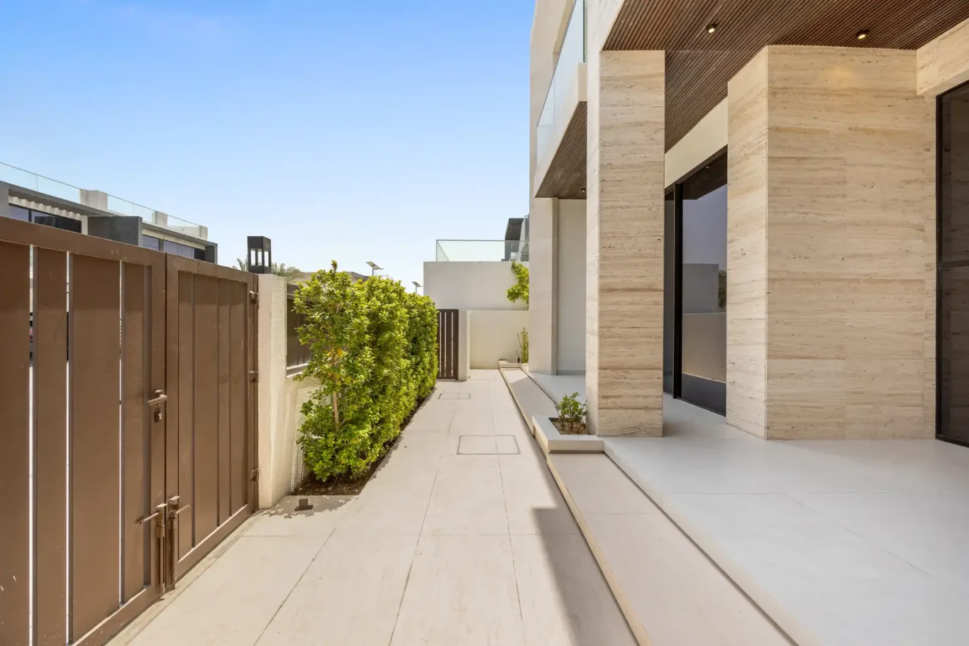 Side entrance with a wooden gate and travertine facade, unfurnished five-bedroom villa in Al Furjan, Dubai.