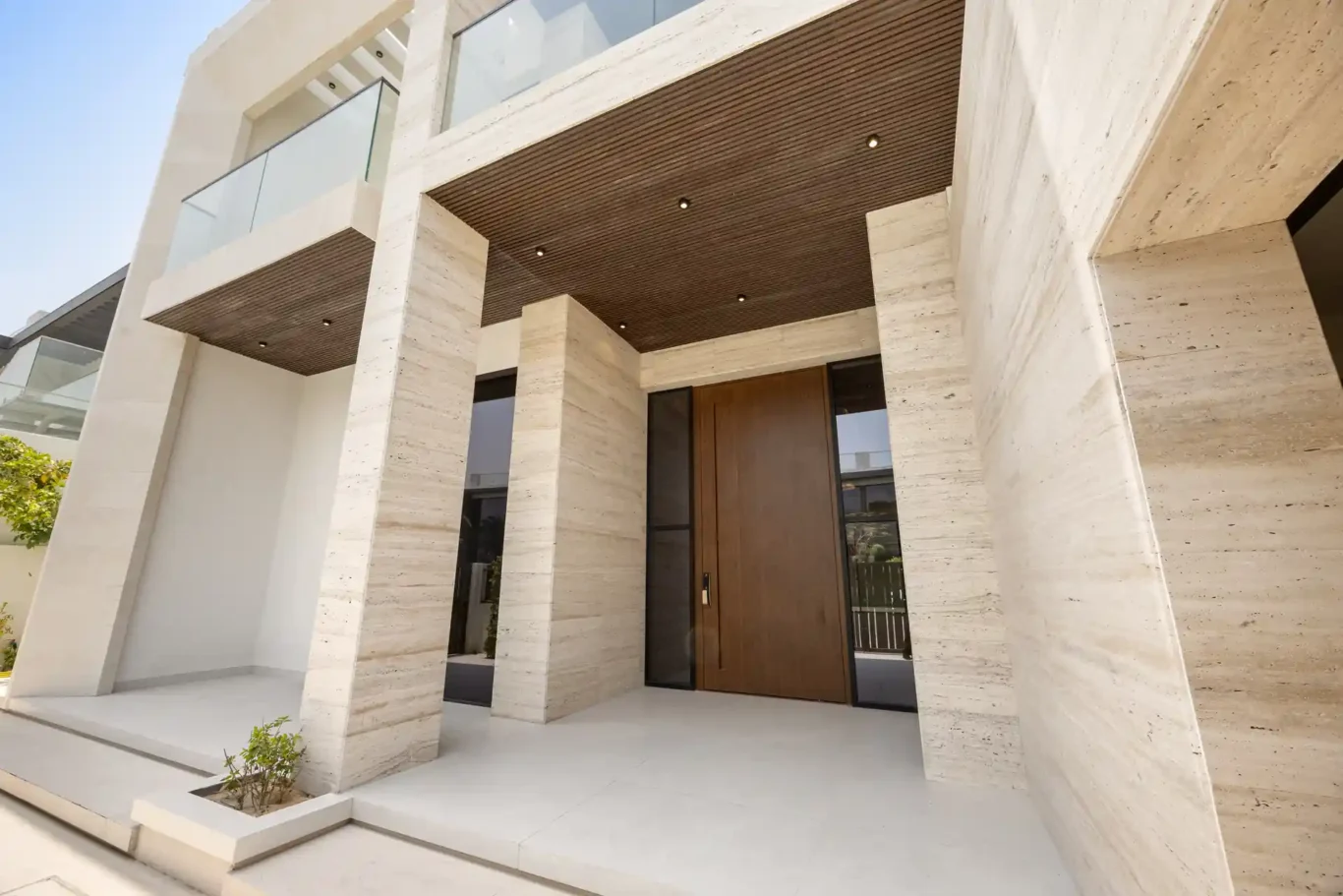 Front entrance with travertine columns and a wood door, unfurnished five-bedroom villa in Al Furjan, Dubai.
