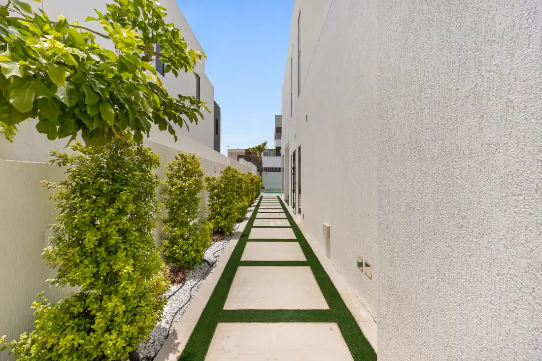 Side passage with stepping stones and a green hedge, unfurnished five-bedroom villa in Al Furjan, Dubai.